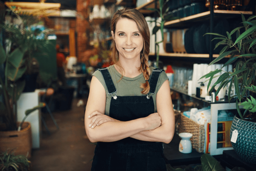 A confident female business owner standing with arms crossed in her store, representing a success business strategy through entrepreneurial leadership and growth.