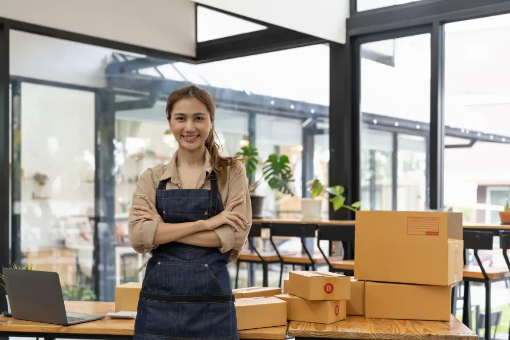 Emprendedora en su oficina rodeada de cajas, mostrando los beneficios de implementar un CRM en pymes y startups para mejorar la gestión de clientes y pedidos.