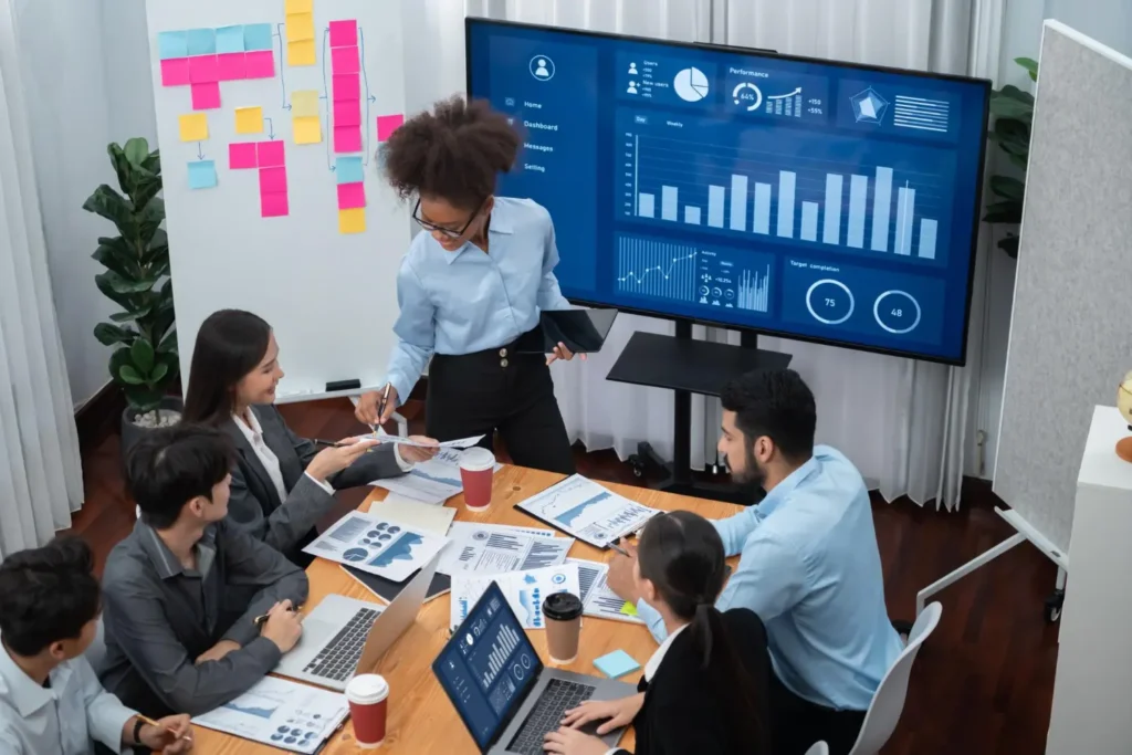 Equipo de profesionales en una reunión de trabajo discutiendo cómo implementar un CRM en una pyme, utilizando gráficos y análisis de datos en pantalla.