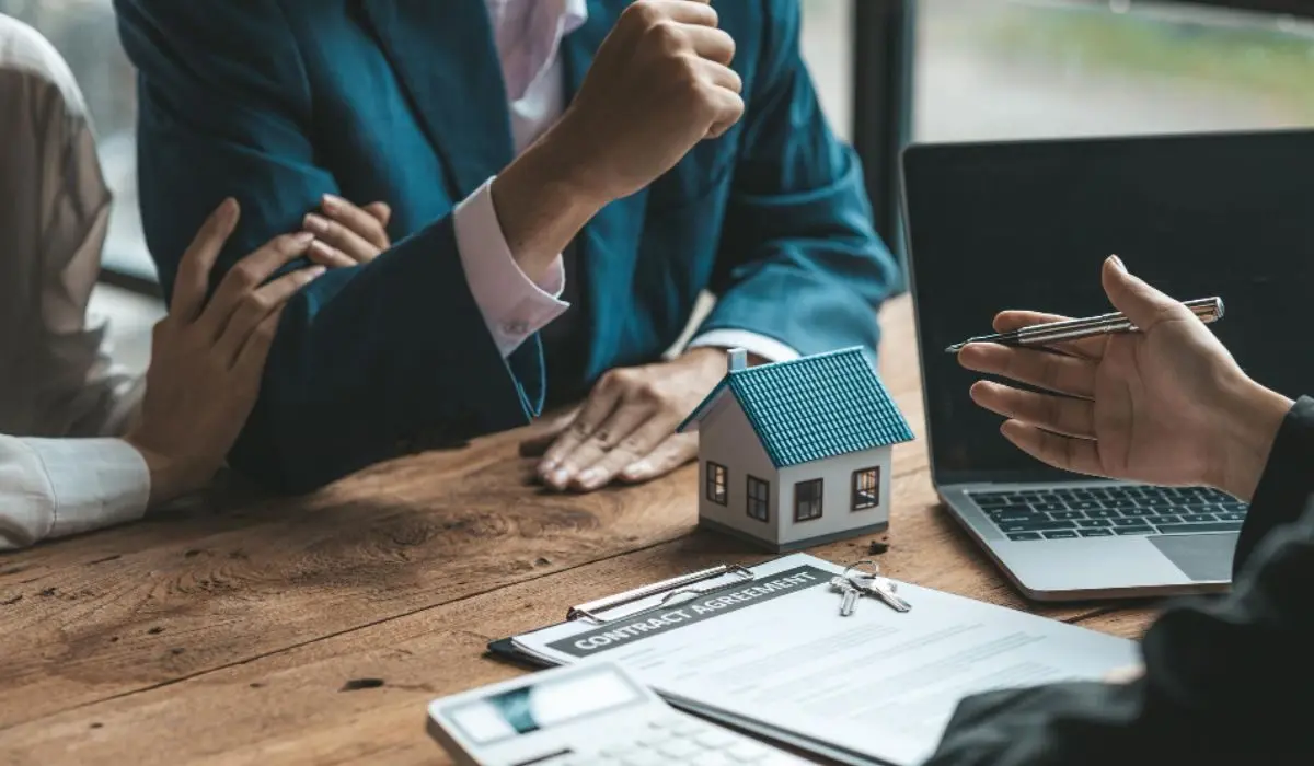 Personas en una reunión inmobiliaria discutiendo un contrato de compra, con un modelo de casa en miniatura y llaves sobre la mesa, representando diferentes tipos de clientes de una inmobiliaria.