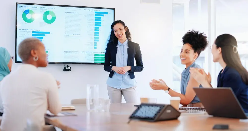 Manager de CRM en agencia de bienes raíces presentando datos de clientes en una pantalla durante reunión de equipo, optimizando estrategias de ventas y gestión de relaciones