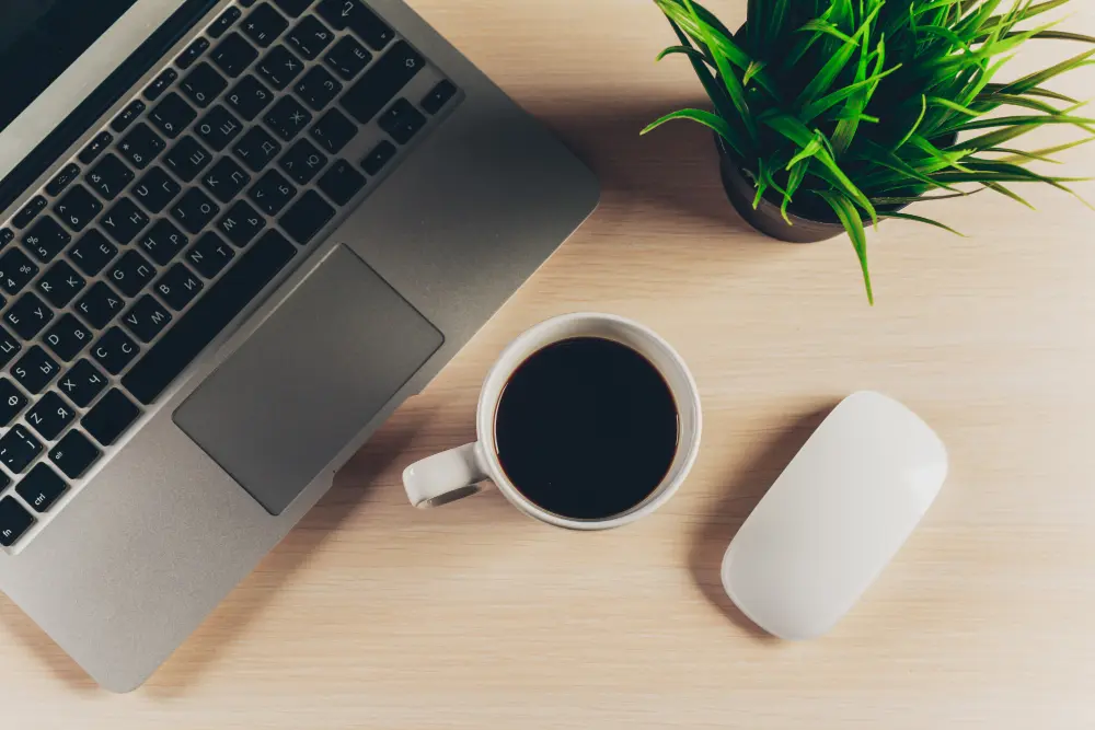 Laptop, taza de café y mouse sobre escritorio de madera, representando estrategias de redes sociales para trabajo digital y marketing online.