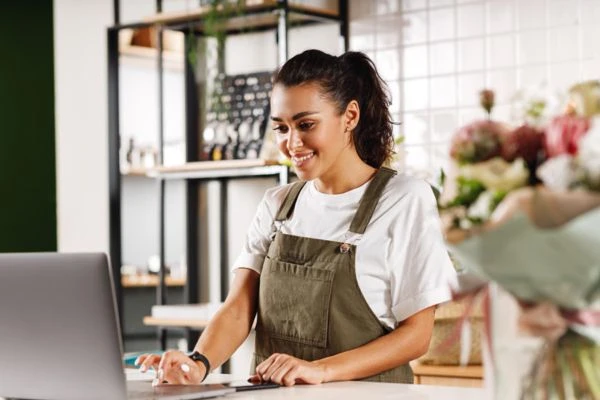 Emprendedora usando CRM para pymes en una laptop en su tienda para gestionar clientes.