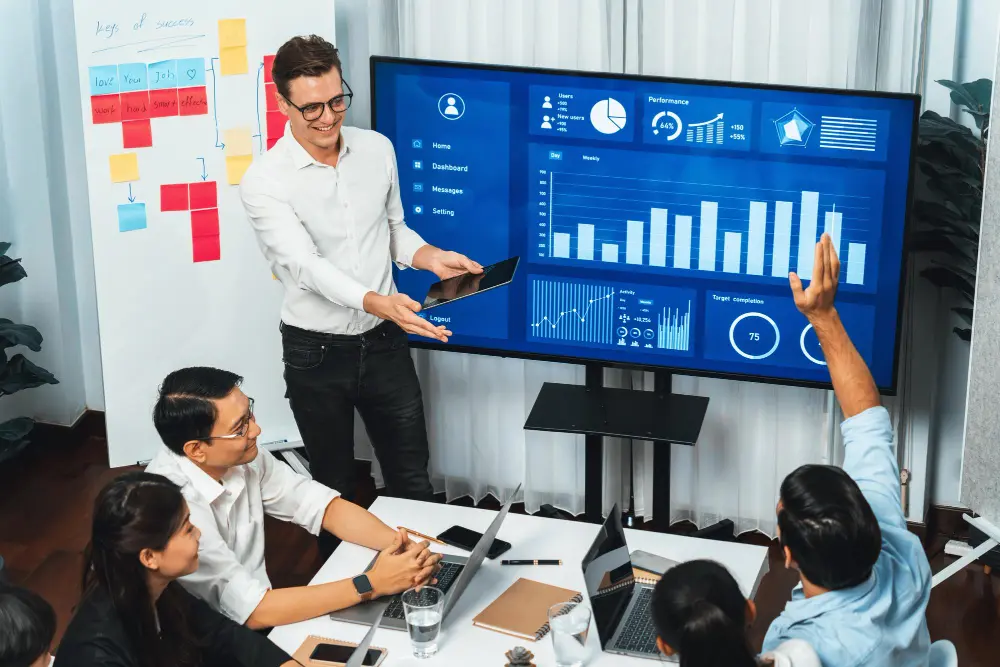 Equipo en reunión analizando panel de métricas en pantalla, mostrando beneficios del CRM y automatización.