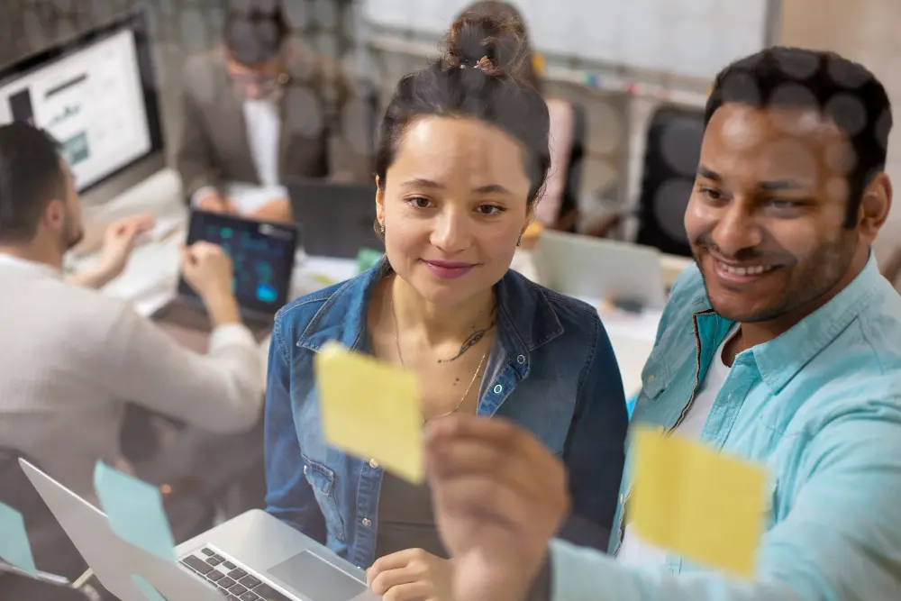 Dos colegas revisan notas adhesivas para organizar tareas de implementación de CRM en empresas en la oficina.